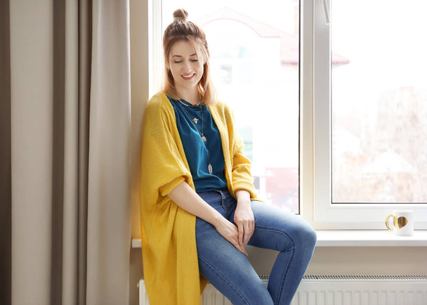 Young woman in yellow cardigan near window indoors - Photo, image