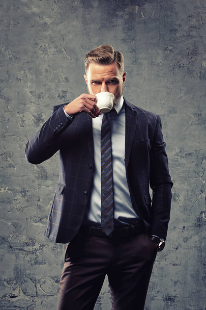 Brutal man drinking coffee against grey wall - Foto, afbeelding