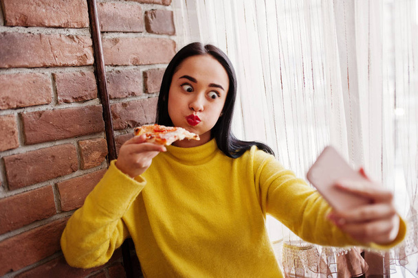 Funny brunette girl in yellow sweater eating pizza at restaurant - Foto, Imagem