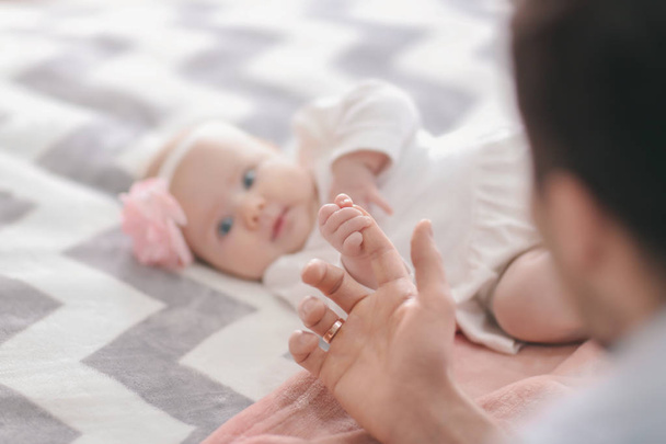 Cute baby holding father's finger on bed - Fotó, kép