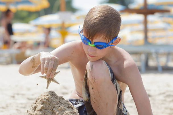 Concentrated beach boy building sand castle with starfish on top - Photo, Image