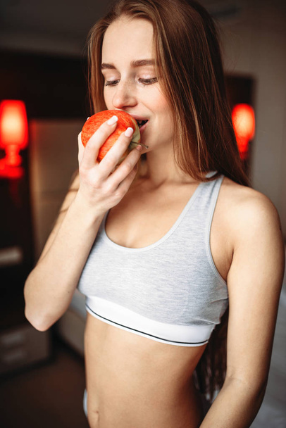 mujer joven en ropa interior comiendo manzana fresca en la mañana
 - Foto, Imagen