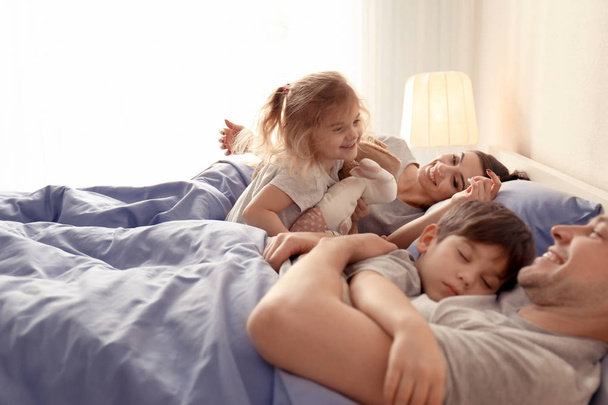 Cute awaken girl playing near sleeping family on bed at home - Foto, Bild