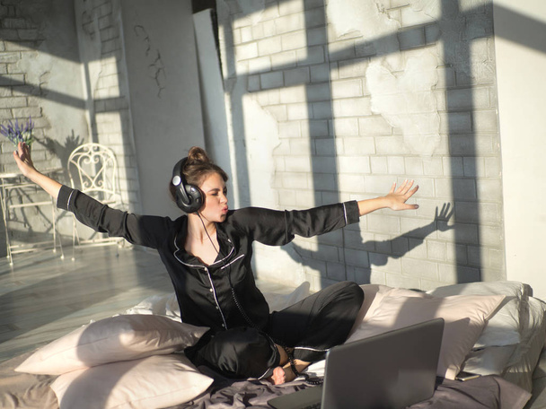Ευτυχισμένη γυναίκα ή εφηβικό κορίτσι ακουστικά να ακούτε μουσική από το φορητό υπολογιστή και να χορεύουν στο κρεβάτι - Φωτογραφία, εικόνα