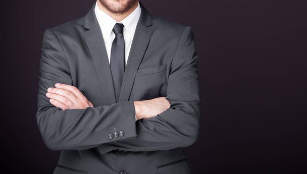 Businessman standing with arms crossed on black background - Fotó, kép