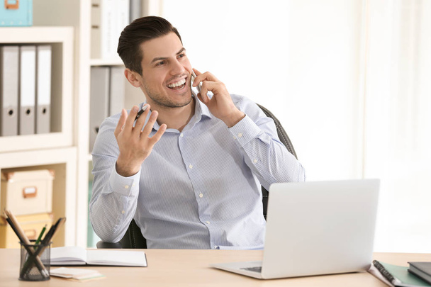 Young man talking on mobile phone while working in office - Foto, afbeelding