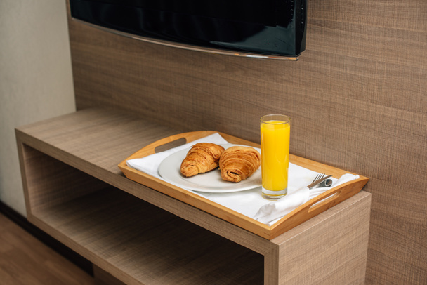 croissants en sinaasappelsap op houten dienblad - Foto, afbeelding