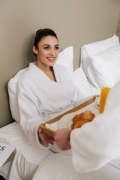 beautiful woman in bathrobe taking food on tray from man while relaxing in bed - Fotografie, Obrázek