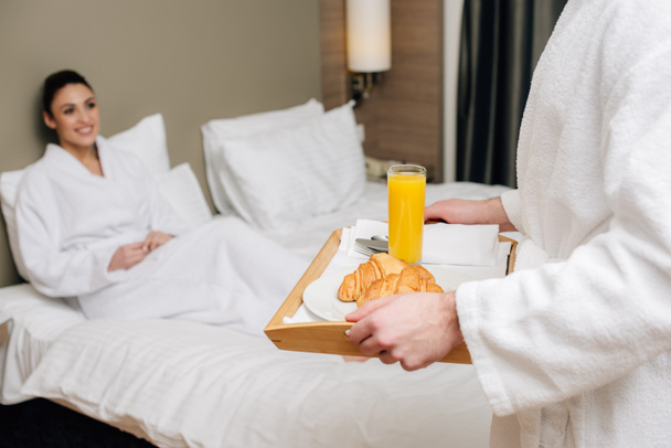 cropped shot of man carrying tray with breakfast for girlfriend while she sitting in bed at hotel suite - Фото, изображение