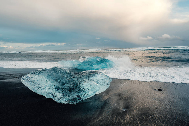 Gelo na praia vulcânica negra perto da lagoa do glaciar Jokulsarlon, no inverno da Islândia. Detalhe de um fragmento glacial de gelo na praia de areia preta na bela luz da noite
. - Foto, Imagem