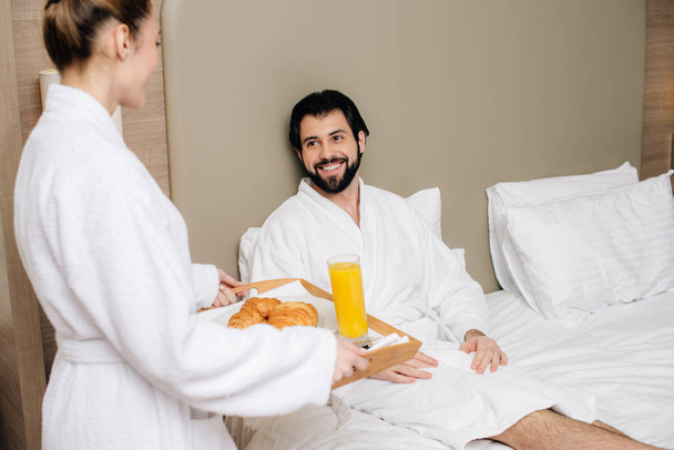 woman carrying tray with breakfast for boyfriend in hotel suite - Photo, Image