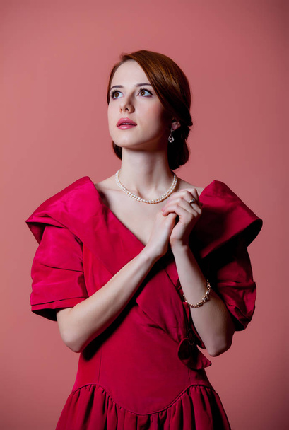 Młoda Ruda Kobieta w czerwonym epoki wiktoriańskiej ubrania na różowym tle  - Zdjęcie, obraz