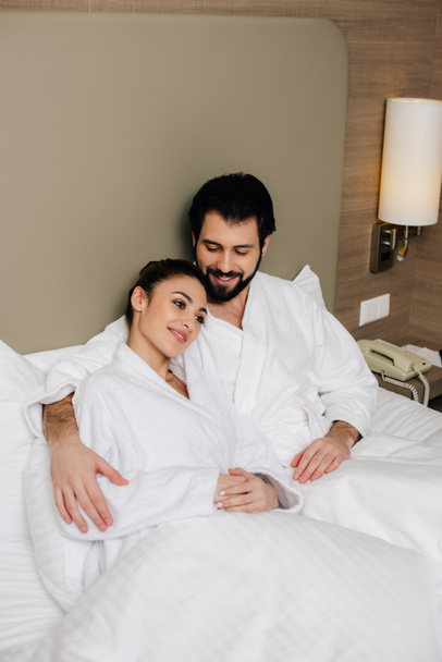 счастливая пара в халатах, обнимающаяся в постели гостиничного номера
 - Фото, изображение