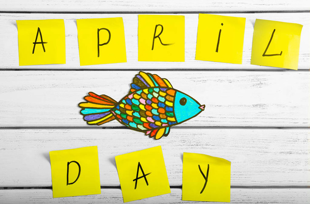 Notes with phrase "April day" and drawing of fish on wooden background - Фото, изображение