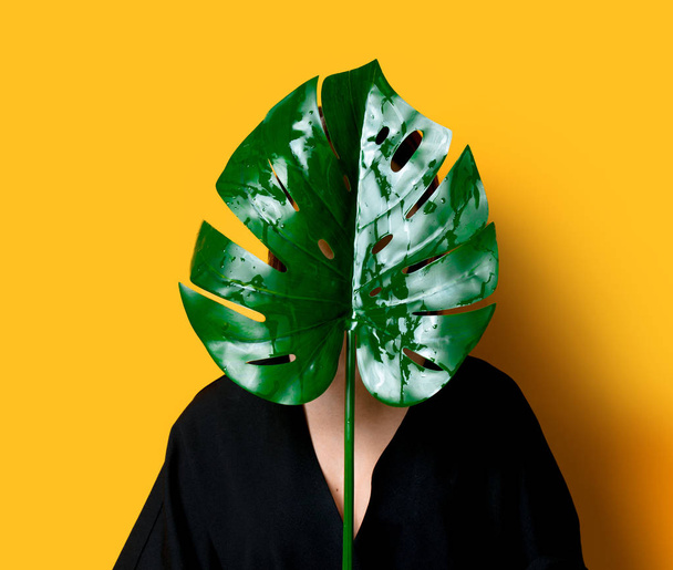 Beautiful woman in dark clothes with palm leaf on yellow color background - Fotó, kép