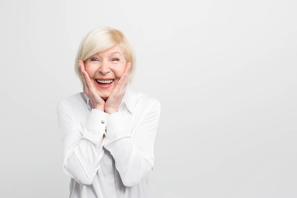 Old but happy woman wears white blouse and showing that she is ery surprised. She has a good luck. Isolated on white background. - Fotografie, Obrázek