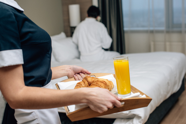 cropped shot of maid in uniform holding tray with croissants and juice for hotel guest - Foto, Imagem