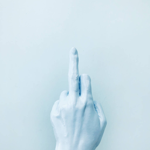 La mano en pintura azul muestra un gesto agresivo con el dedo medio. Estilo de moda mínimo
. - Foto, imagen