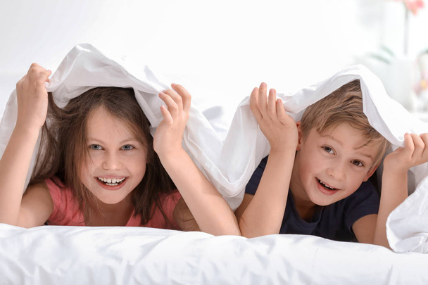 Portrait of happy little brother and sister lying on bed under blanket - Фото, изображение