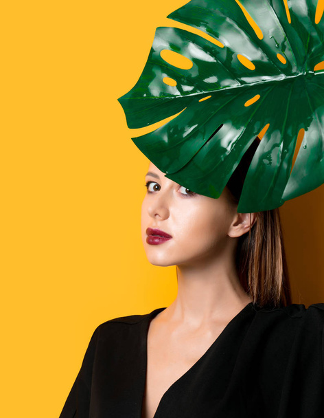 Beautiful woman in dark clothes with palm leaf on yellow color background - Φωτογραφία, εικόνα