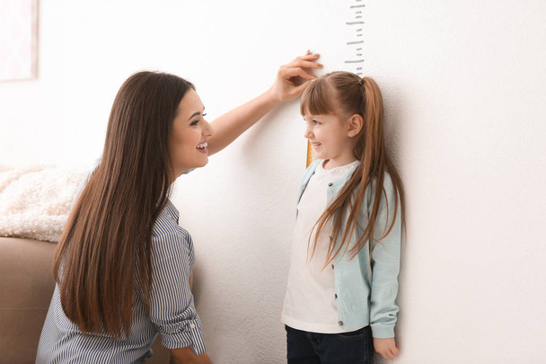 Young woman measuring her daughter's height indoors - Фото, зображення
