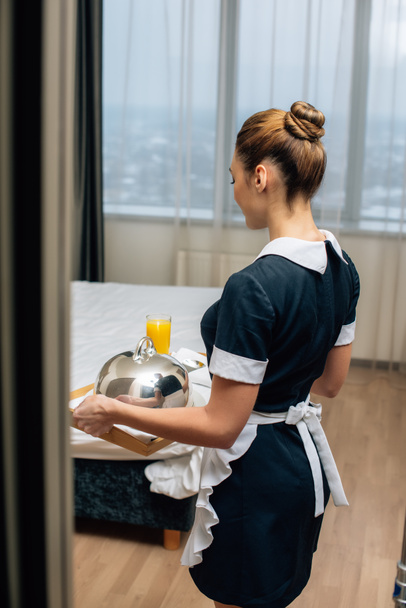 giovane cameriera attraente in uniforme che tiene la colazione coperta di cloche sul vassoio
 - Foto, immagini
