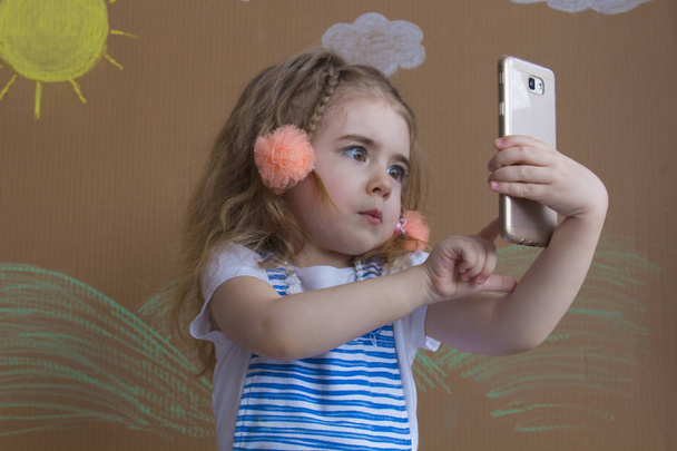 portrait cute girl makes selfie with a cell phone. Adorable smiling toddler kid taking a selfie photo with smartphone - Foto, Imagen