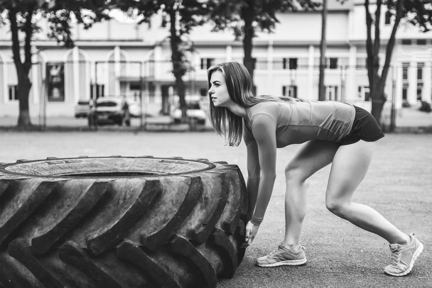 Young sporty girl working out outdoor with big tire in summer park - Foto, Imagen