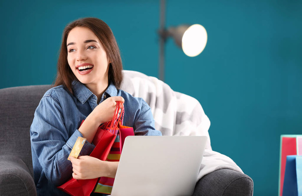 Young woman shopping online with credit card and laptop in armchair - Photo, Image