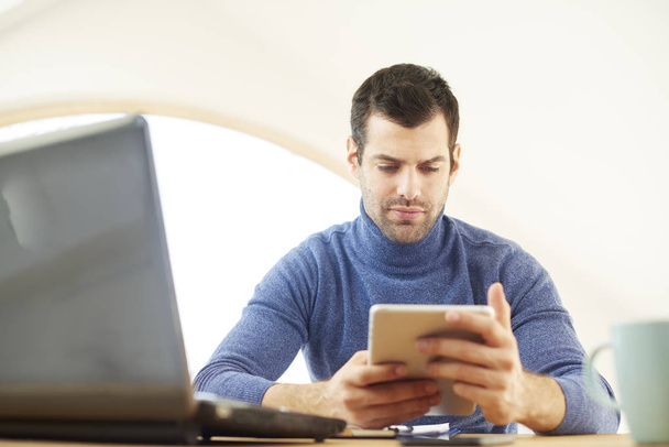 Young man wearing turtleneck sweater while using digital tablet and laptop at home. Home office. - Foto, Imagen