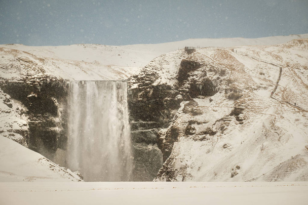 Skogafoss, the great and beautiful waterfall in Iceland during winter. Snow blizzard in Iceland near famous Skogafoss waterfall. - Fotó, kép