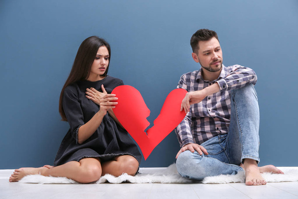 Young couple tearing paper heart in half near color wall. Relationship problems - Photo, image