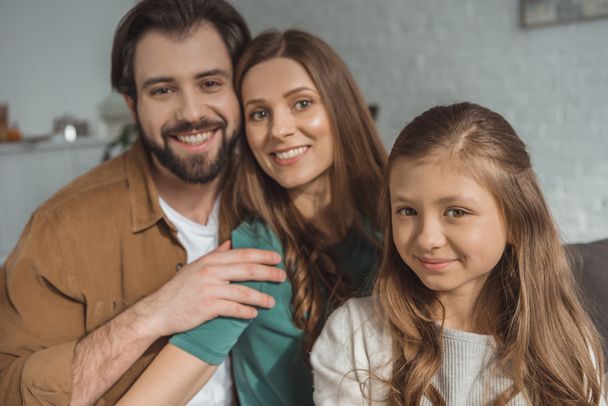 smiling parents and daughter looking at camera at home - Fotografie, Obrázek