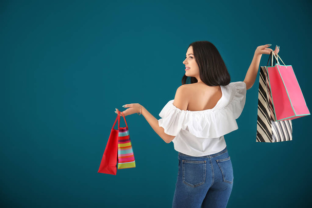Happy young woman with shopping bags on color background - Фото, зображення