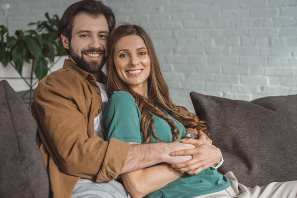smiling boyfriend hugging girlfriend and they looking at camera at home - Фото, зображення