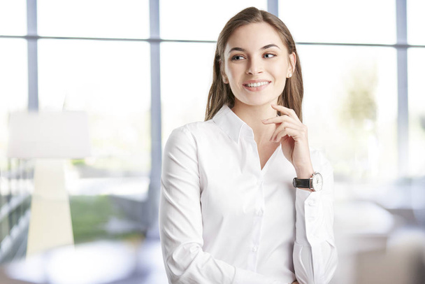 Smiling young businesswoman wearing white shirt and looking away while standing at the office. - Fotoğraf, Görsel