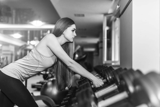 Beautiful young lady with long hair training in gym. Young woman exercising with fitness equipment - Φωτογραφία, εικόνα