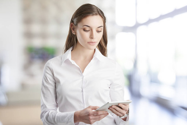 Retrato de una joven mujer de negocios asistente de finanzas usando tableta digital mientras está de pie en la oficina
.  - Foto, Imagen