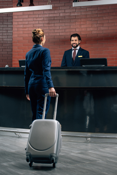 business woman with luggage going at hotel reception counter
 - Фото, изображение