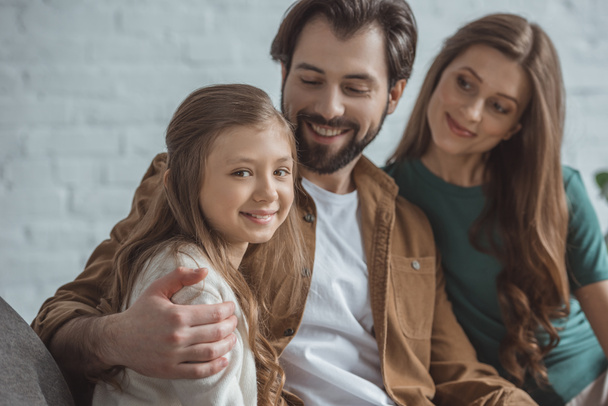 smiling daughter sitting with parents on sofa at home - Φωτογραφία, εικόνα