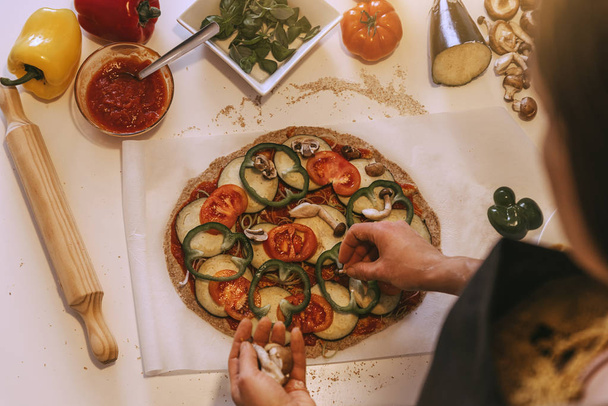Woman adding healthy ingredients to pizza. - Zdjęcie, obraz