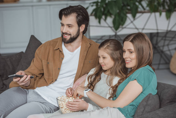 happy parents and daughter watching tv with popcorn at home - Fotó, kép