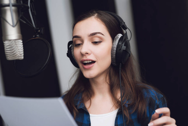 The girl in the recording studio sings a song. Her headphones are on her head. Next to her is a microphone. She emotionally sings the song. - Fotoğraf, Görsel