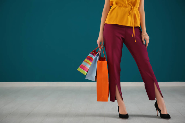 Young woman with shopping bags against color wall - Foto, imagen