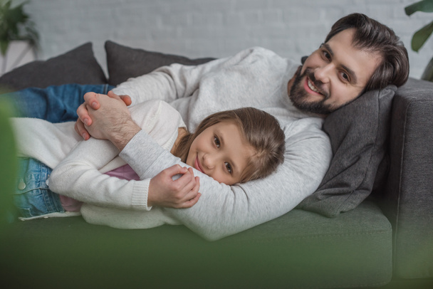 father and daughter lying on sofa and looking at camera  - 写真・画像