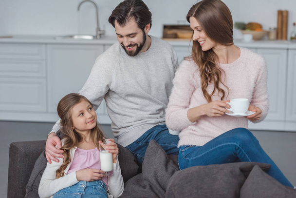 parents and daughter with milk and coffee on sofa - Foto, immagini
