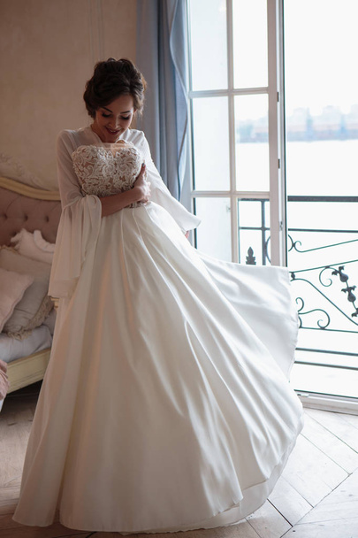 Beautiful bride in a white wedding peignoir in a morning. beauty portrait in interior - Foto, Imagen