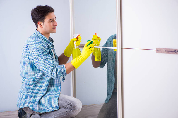 Jeune homme nettoyage miroir à la maison hôtel - Photo, image