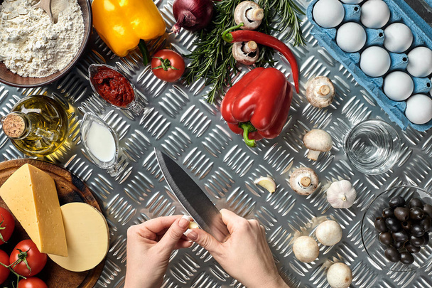 Női kézzel kés fém konyhaasztalon, ezen a környéken: hazugság alapanyagok, zöldségek és fűszerek pizza. - Fotó, kép