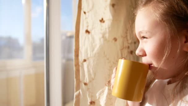 kleines Mädchen trinkt bei Sonnenaufgang Tee in der Nähe von Fenstern - Filmmaterial, Video